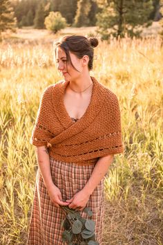 a woman standing in the middle of a field wearing a brown wrap around her neck