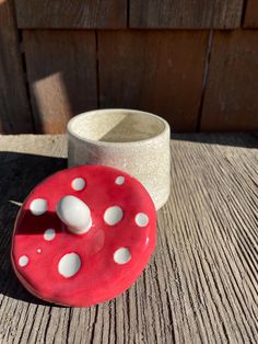 a red and white object sitting on top of a wooden table next to a cup