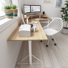 a desk with a computer, chair and plant on it in front of a window