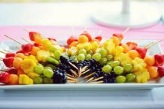 a white plate topped with fruit and skewers on top of a pink table cloth