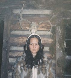 a woman standing in front of a wooden wall with deer heads on it's head