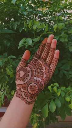 a hand with henna on it next to a bush and trees in the background