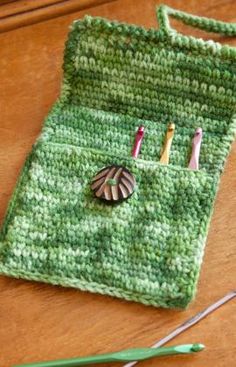 a green crochet bag with pins and needles in it on a wooden table