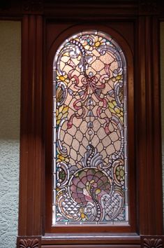 an ornate stained glass window in the corner of a room with white walls and wood trim