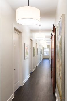 a long hallway with white walls and wood floors is lit by a round light fixture