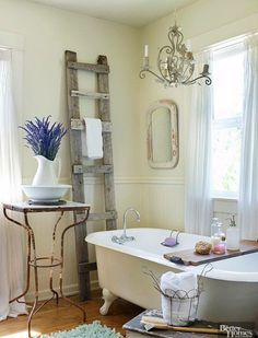 a white bath tub sitting under a window next to a wooden ladder in a bathroom