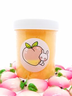 a jar of peach jam sitting on top of pink and white balls with green leaves around it