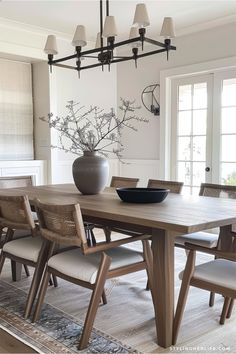 a dining room table with chairs and a vase on it's centerpiece in front of a window