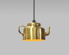 a brass teapot hanging from a black cord on a gray background with a yellow light in the middle