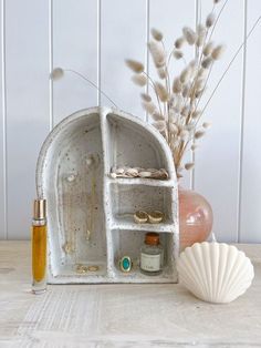 a white shelf with some jewelry on top of it next to a vase and seashell