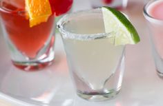 three different types of cocktails on a white plate with orange slices and lime wedge