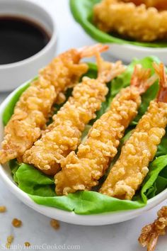 two white bowls filled with fried shrimp and lettuce next to dipping sauces