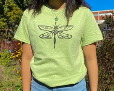 -100% Ultra cotton Gildan T-shirt (color: green) -Comfy cotton T with dragonfly print in black/white fabric ink -machine washable (no heat) -hand carved original print design -models wearing a unisex size small (first model is 5'2 & second model is 5'6) -message for more sizing options -message me with any questions or if you want anything custom Cheap Green Tops With Cartoon Print, Cheap Green Graphic Print Short Sleeve Shirt, Cheap Green Tops With Vintage Print, Cheap Artsy Tops With Graphic Print, Cheap Green Shirt With Logo Print, Cheap Casual Dinosaur Print Tops, Cheap Green Grunge Tops, Cheap Green T-shirt For Layering, Cheap Green Distressed Tops