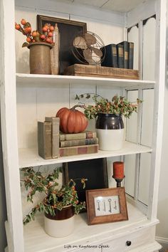 a white book shelf with pumpkins, books and other items on top of it