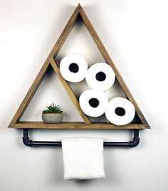 a triangle shaped shelf with three rolls of toilet paper on it and a potted plant in the corner