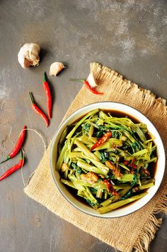 a white bowl filled with green beans and red peppers next to garlic on top of a table