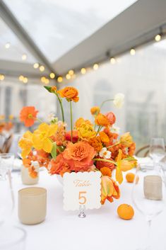 the table is set with orange and white flowers in vases, plates and glasses