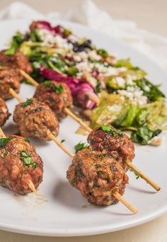 meatballs and salad on skewers with toothpicks sitting on a white plate