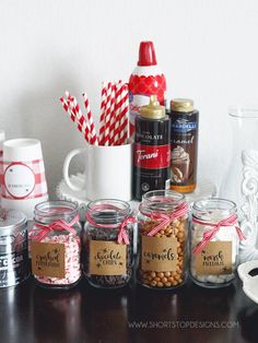 there are many jars with candy in them on the table next to cups and mugs