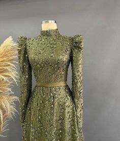 a green dress with gold sequins on it and a plant next to it