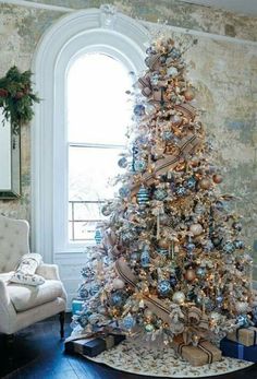 a decorated christmas tree in the corner of a room with a chair and large window