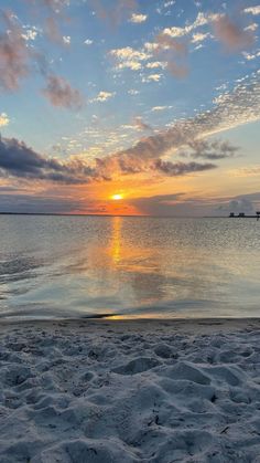 the sun is setting over the ocean with clouds in the sky and sand on the beach