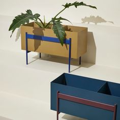 two planters sitting next to each other on top of a white floor and one has a green plant in it