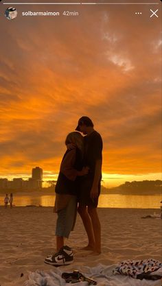 two people embracing each other on the beach at sunset, with an orange sky in the background