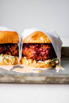 two burgers sitting on top of a metal tray covered in wax paper wrappers