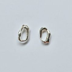 two small silver earrings on a white surface