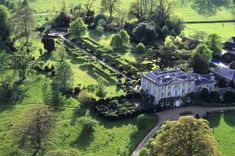 an aerial view of a large white house surrounded by trees and lush green field area