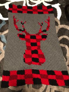 a crocheted blanket with a red and black deer on it's back