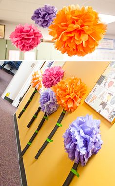 several different types of paper flowers are hanging from the ceiling and on the table in front of them