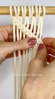 two hands are working on an object that is white and has braided strings attached to it