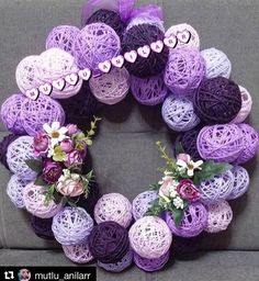 a wreath made out of yarn with flowers and hearts on the front, sitting on a couch