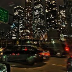 the city skyline is lit up at night, with cars driving down the street in front of it