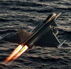 a fighter jet flying over the ocean with it's landing gear on its side