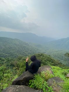 a person sitting on top of a large rock in the middle of a lush green forest