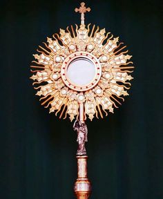 an ornate gold clock on top of a wooden pole in front of a black background