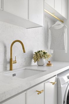 a washer and dryer in a white laundry room with gold faucets