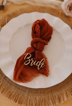 a white plate topped with a red scarf and the word bride written in cursive writing