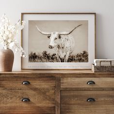 a cow with long horns standing on top of a dresser next to a flower vase