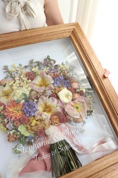 a woman holding a framed floral arrangement in her hands