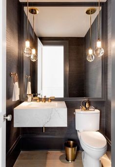 a white toilet sitting next to a sink in a bathroom under two hanging light bulbs