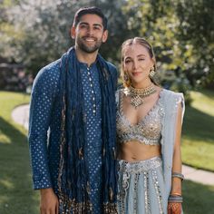 a man and woman standing next to each other in front of some trees with grass