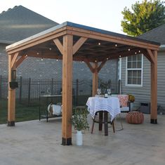 a covered patio with table and chairs in front of a fenced backyard area at dusk