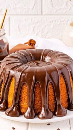 a bundt cake with chocolate icing on a white plate next to a jar of peanut butter