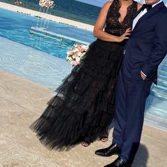 a man and woman standing next to each other in front of a pool with an ocean view