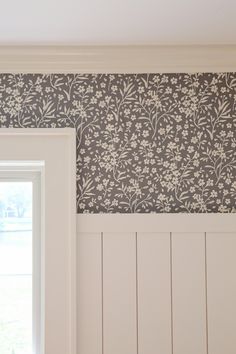 an empty room with white paneling and floral wallpaper on the walls, next to a window