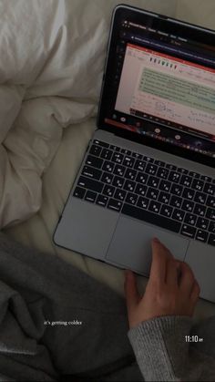 a person using a laptop computer on top of a white bed covered in pillows and blankets